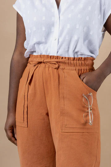Person wearing a white blouse with small patterns made using Sepia Pants and Shorts sewing pattern and rust-colored pants on a beige background