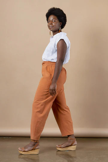 Woman wearing a white top and orange pants made using Sepia Pants and Shorts sewing pattern against a beige background