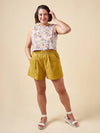 Woman wearing a floral top and yellow shorts made using Sepia Pants and Shorts sewing patternagainst a beige background