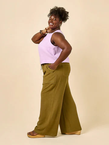 Woman wearing a light purple sleeveless top and green wide-leg pants made using Sepia Pants and Shorts sewing pattern on a beige background
