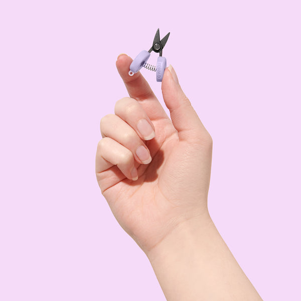 Hand holding a small pair of purple nail clippers against a light purple background
