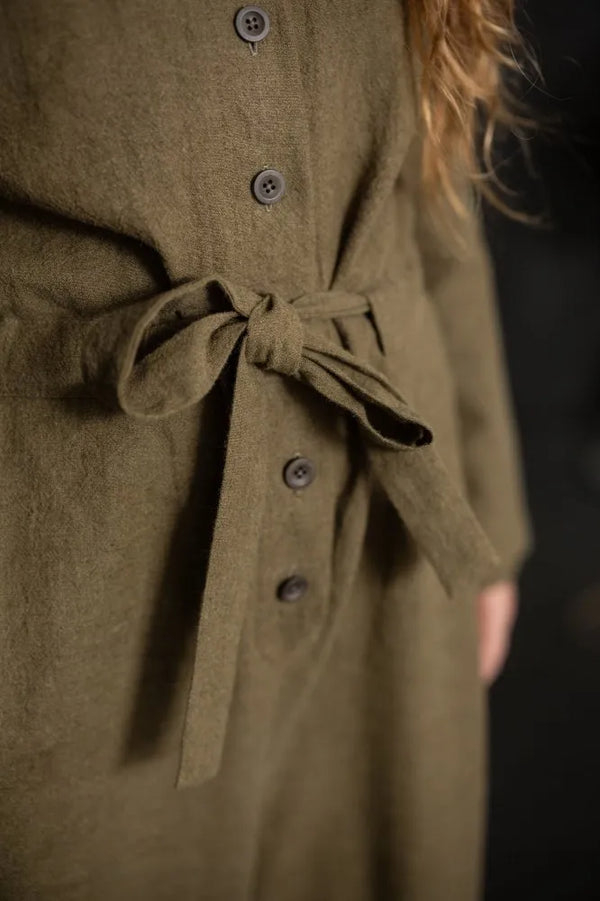 Close-up of a person wearing a brown coat with a belt, on a dark background