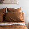Tobacco brown linen pillowcases set on a bed with a neutral wall and framed picture in the background