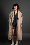 Woman wearing a long beige coat over a striped outfit on a dark background