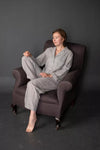 Woman in gray pajamas sitting on a brown armchair against a dark background