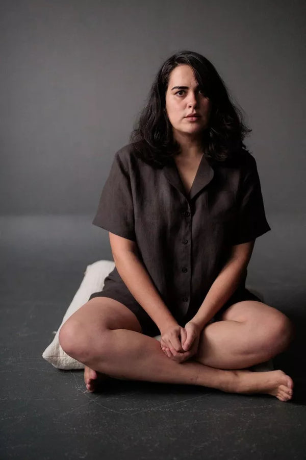 Woman sitting cross-legged on a dark surface with a gray background