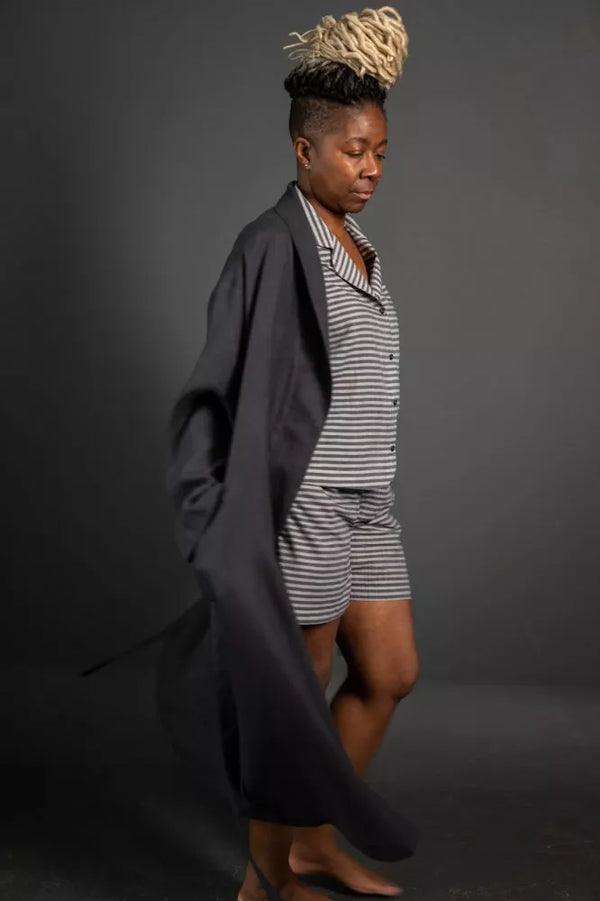 Person wearing a striped outfit with a long dark garment against a gray background