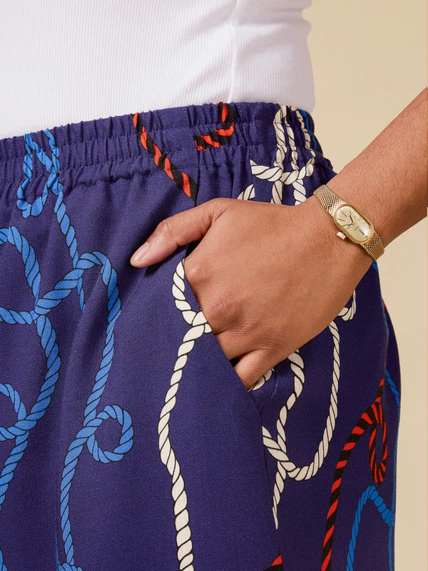 Person wearing a navy blue pants with rope pattern and white shirt, hand in pocket.