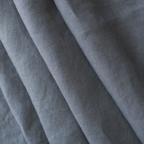 A close-up of draped gray fabric with a visible woven texture, arranged in soft diagonal folds.