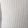 Close-up of a white pillow with brown stripes and a blurred vase in the background.
