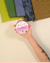 Hand holding a roll of fabric tape with colorful fabrics in the background