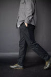 Person wearing a gray shirt and black pants against a dark background