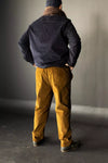 Person wearing a dark jacket and mustard The Elling Men’s Trouser standing against a plain background