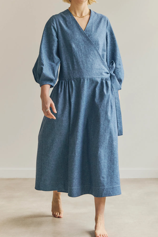 Woman wearing a blue malie Wrap Dress made with PDF sewing patternagainst a plain background