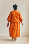 Person wearing an orange malie Wrap Dress made with PDF sewing pattern standing against a plain background