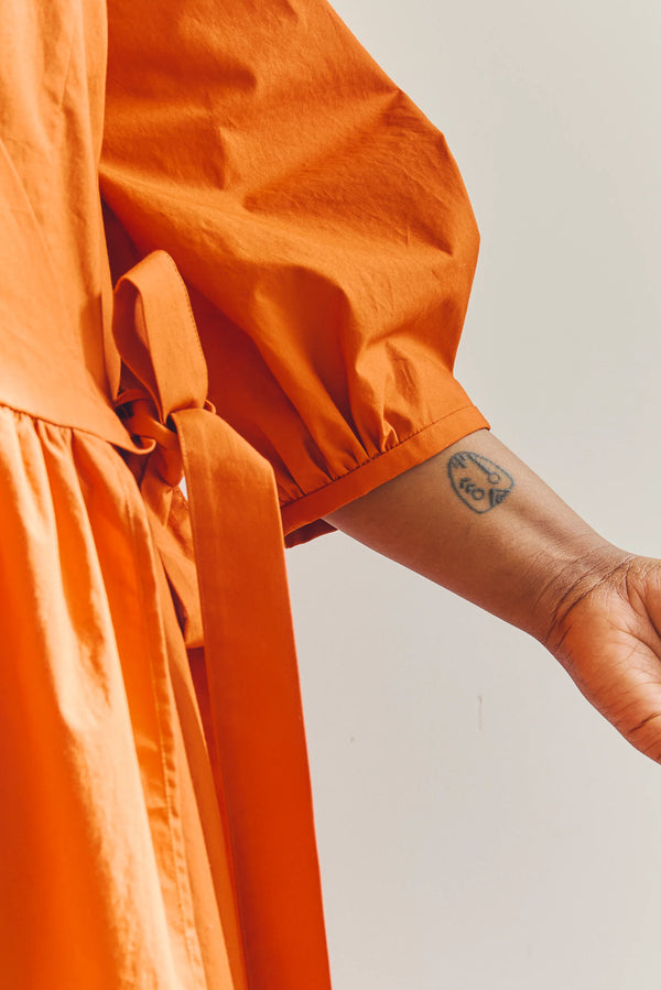 Person wearing an orange malie Wrap Dress made with PDF sewing patternwith a plain background