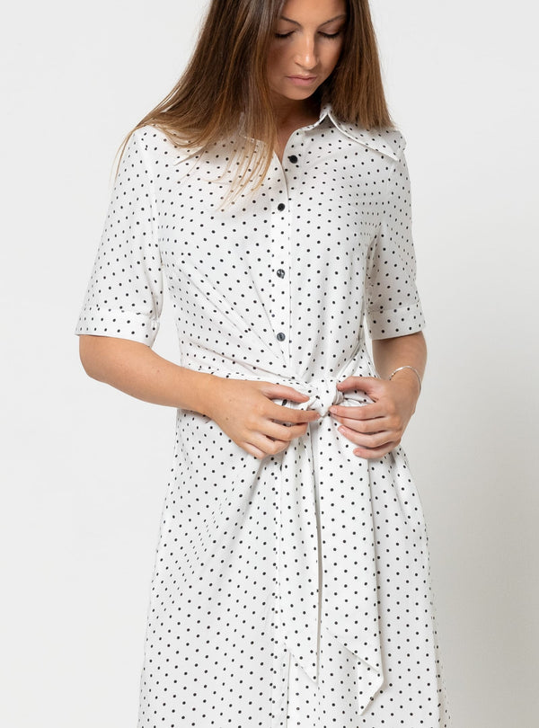 Woman wearing a white dress with black polka dots made using Avon Woven Shirt and Dress sewing patternon a plain background