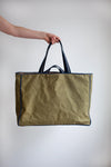 Person holding a green tote bag with black handles made using the Away Tote PDF Sewing Patternagainst a plain background