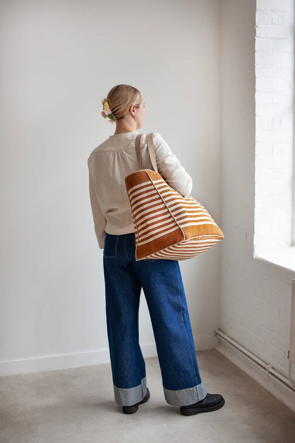 Person holding a striped bag made using the Away Tote PDF Sewing Patternin a minimalistic room with a window.