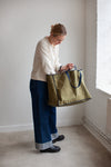 Person holding a green bag made using the Away Tote PDF Sewing Patternin a minimalistic room with white walls and a radiator.