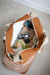 Brown and beige striped bagmade using the Away Tote PDF Sewing Pattern with camera and items on a light gray floor.