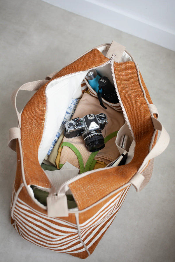 Brown and beige striped bagmade using the Away Tote PDF Sewing Pattern with camera and items on a light gray floor.