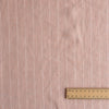 Pink fabric with subtle striped pattern and a wooden ruler for scale on a matching background