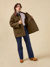 Person wearing a quilted jacket over a white shirt with blue jeans and brown shoes on a beige background