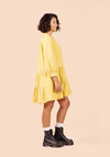 Woman wearing a yellow Poppy Dress with long sleeves on a beige background