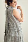 A woman wearing a sleeveless gray and white textured wrap vest with a matching skirt, shown from a side-back angle against a plain light background.