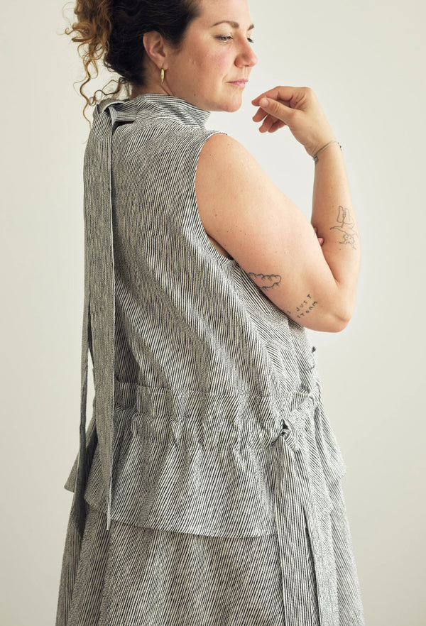 A woman wearing a sleeveless gray and white textured wrap vest with a matching skirt, shown from a side-back angle against a plain light background.