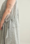 Close-up of a person wearing a sleeveless, textured gray and white striped dress with a tied waist sash, set against a plain light background.