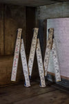 Three vintage tape measures hanging on a wooden surface with a metal grid background.