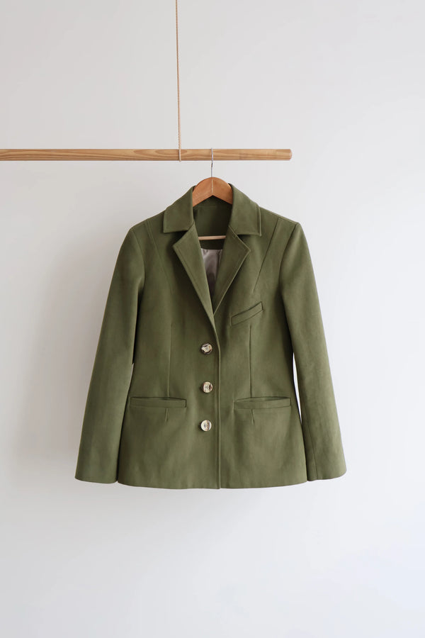 Green jacket made using Naomi Blazer PDF Sewing Pattern on a wooden hanger against a white background
