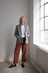 Person wearing a gray blazer made using Naomi Blazer PDF Sewing Patternand brown pants standing in a room with a large window.