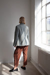 Person wearing a light blue jacket made using Naomi Blazer PDF Sewing Patternand brown pants standing in a room with a large window.