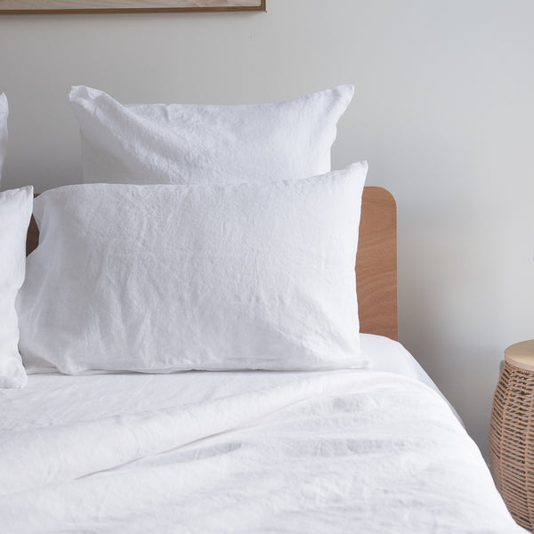 Pure white linenpillows on a bed with a wooden headboard against a plain wall.