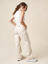 Woman wearing a white sleeveless top and beige cargo pants against a plain background