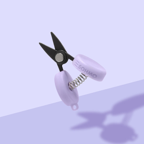 Small scissors with black blades and white handles on a light purple background