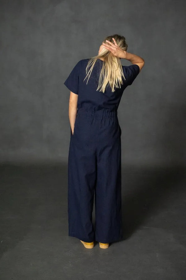 Person wearing a navy bluecassidy jumpsuit against a dark gray background