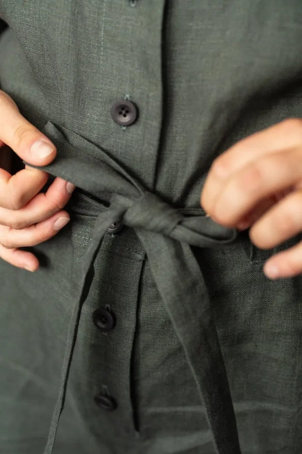 Person adjusting a tie on a dark green shirt with button details.