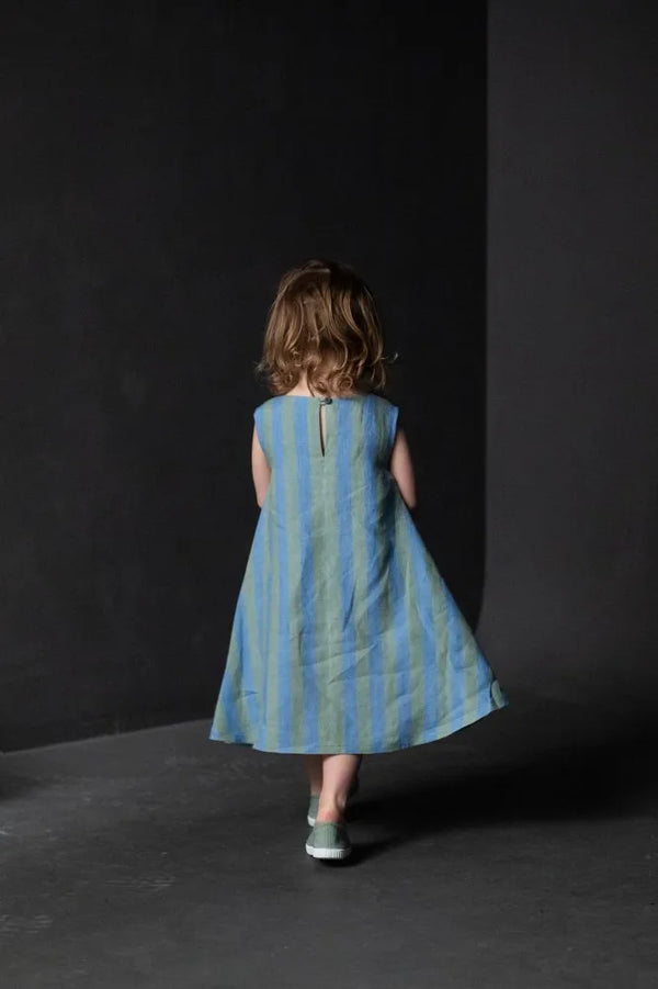 Child wearing a blue striped dress made using trapezette girls dress sewing pattern against a black background