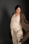 Person wearing a plaid outfit with a brown blanket draped over them against a dark background