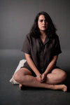 Woman sitting cross-legged on a dark surface with a gray background